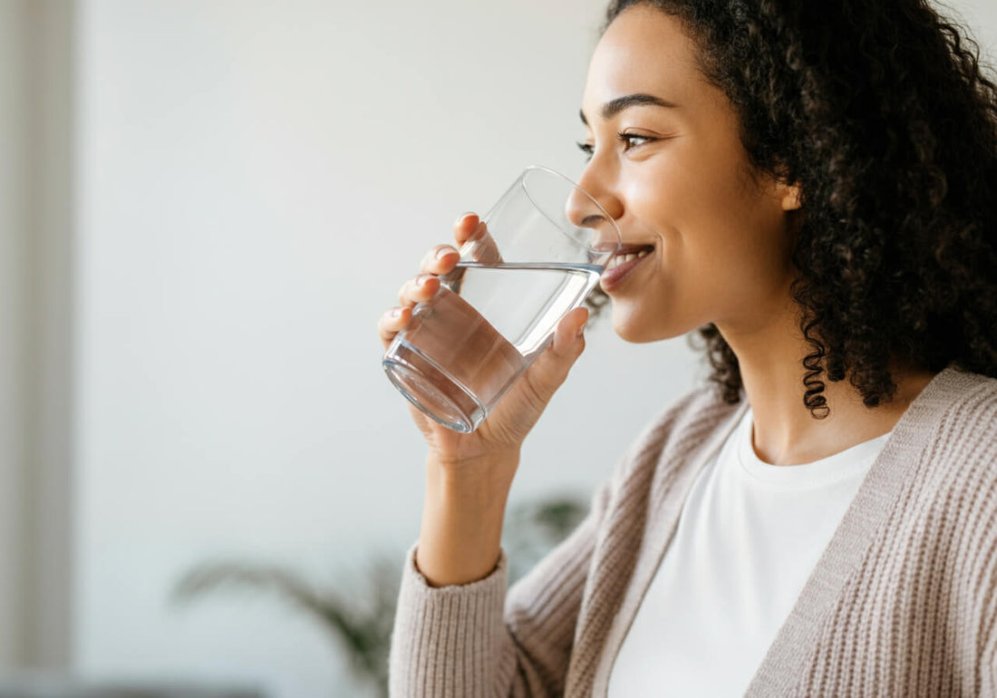 A woman wearing a cardigan over a white shirt drinking from a glass of water