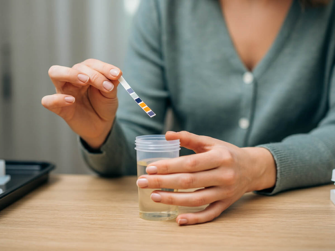 A woman holding a urine test strip on her right hand over the urine cup on his left hand 