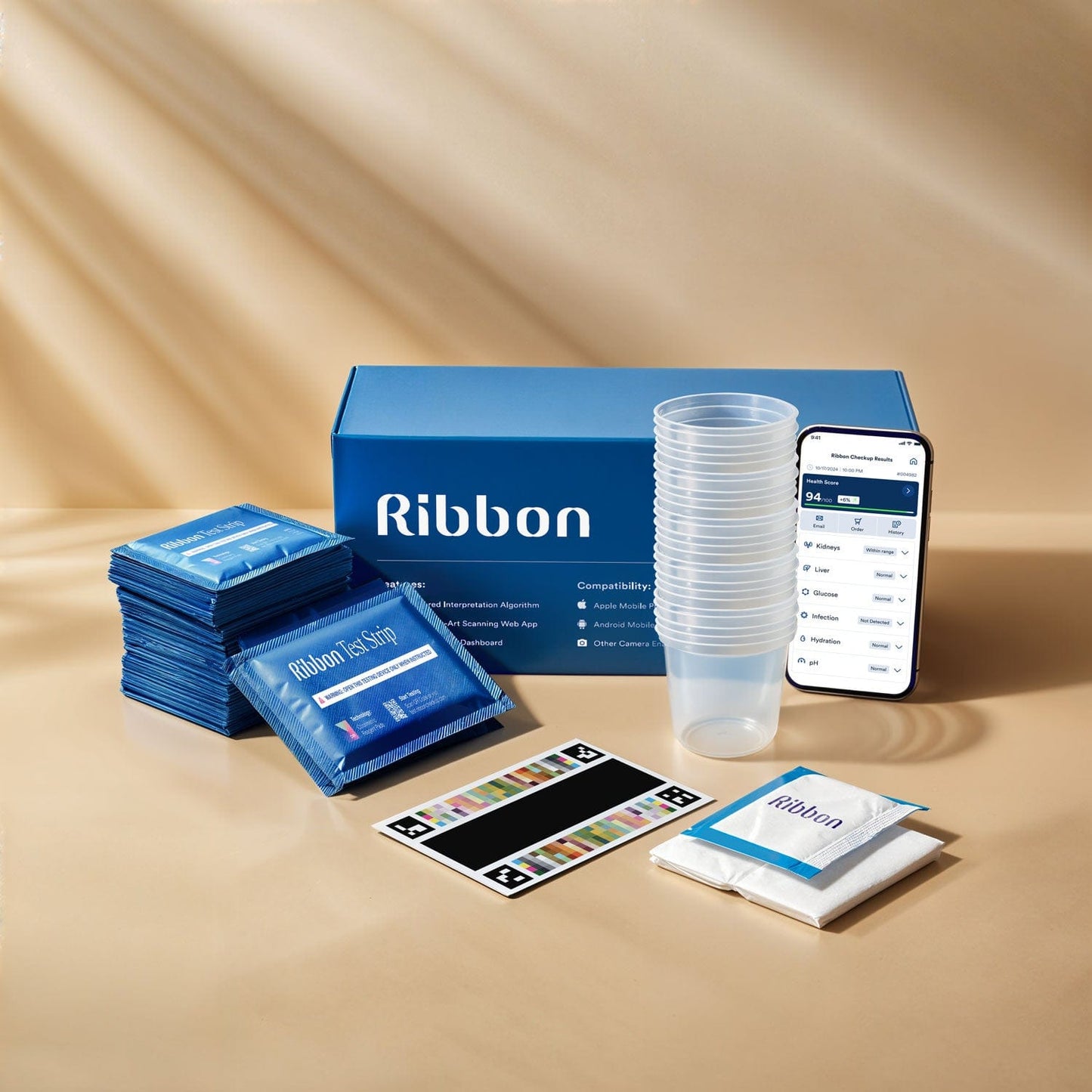 36-pack Ribbon Checkup At-Home Urine Test Kit, stacked test strips, stacked urine cups, tissue papers, a color card, a Ribbon kit box, and a phone with the Ribbon app showing on its screen.